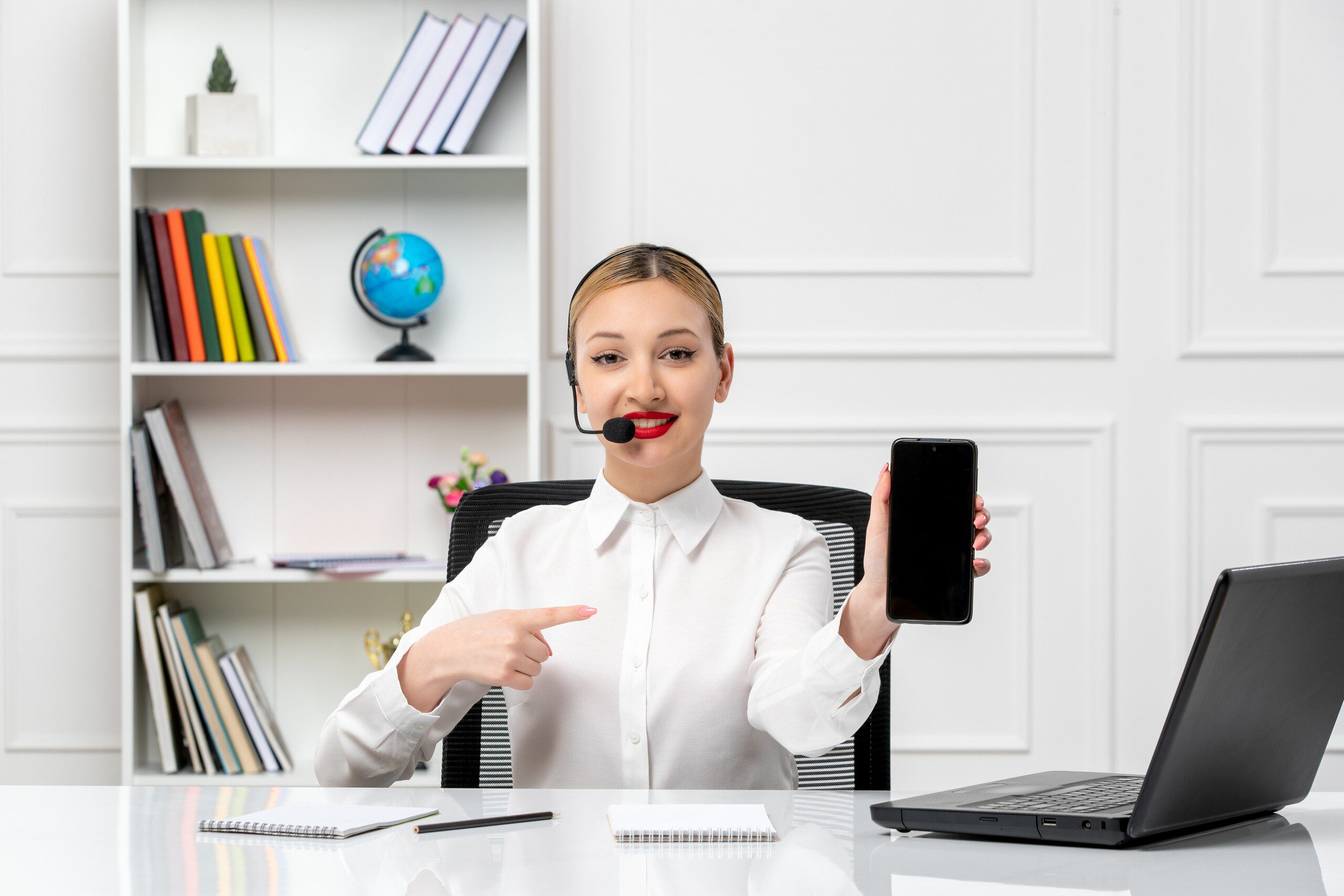 lady with a headset on, sitting at a desk holding a smart phone